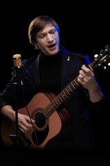 Male musician with guitar in hands playing and posing on black background in blue scenic light