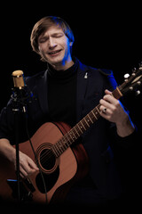 Obraz premium Male musician with guitar in hands playing and posing on black background in blue scenic light
