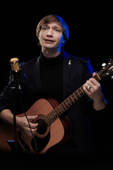 Male musician with guitar in hands playing and posing on black background in blue scenic light