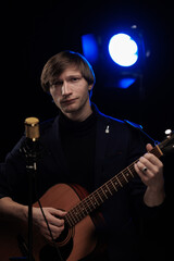 Male musician with guitar in hands playing and posing on black background in blue scenic light