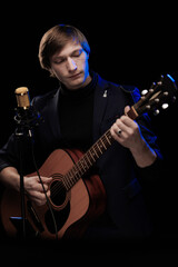 Obraz premium Male musician with guitar in hands playing and posing on black background in blue scenic light