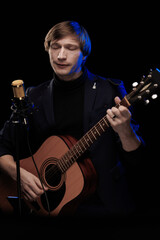 Obraz premium Male musician with guitar in hands playing and posing on black background in blue scenic light