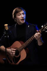Obraz premium Male musician with guitar in hands playing and posing on black background in blue scenic light