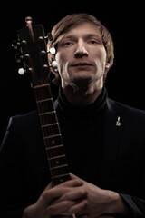 Male musician with guitar in hands playing and posing on black background in blue scenic light