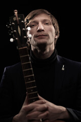 Male musician with guitar in hands playing and posing on black background in blue scenic light