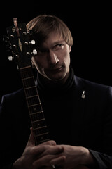 Obraz premium Male musician with guitar in hands playing and posing on black background in blue scenic light