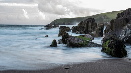 A bay with a sandy beach with a dark clouded sky and green grass and cliffs and a sandy beach at...