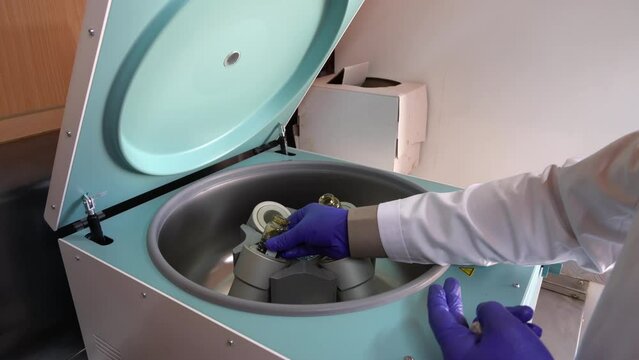 Test tube with oil into centrifuge. Gloved hand lifts beaker and installs to box with centrifuge