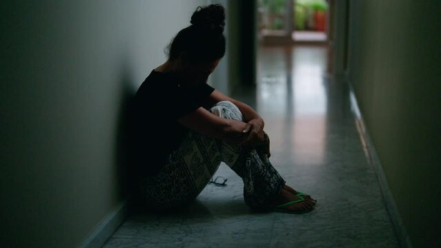 Middle age hispanic woman suffering for domestic violence with bruise on eyes sitting on floor at home