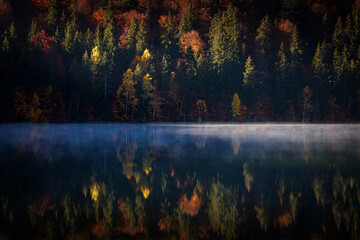 Beautiful colourful landscape in autumn season with rays of light in forest and lake reflection. Romania