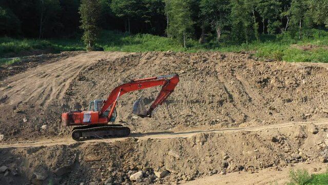 Earthmoving equipment. A red excavator is digging the ground. The bucket of the excavator scoops up the soil against the background of nature. Slow motion.