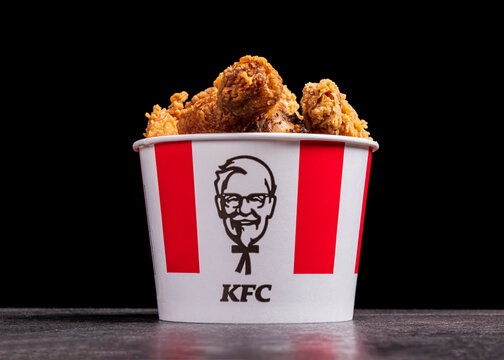 Minsk, Belarus - December 03, 2021: black background, night. Lots of hot wings or strips of KFC chicken in a KFC Kentucky Fried Chicken fast food bucket.