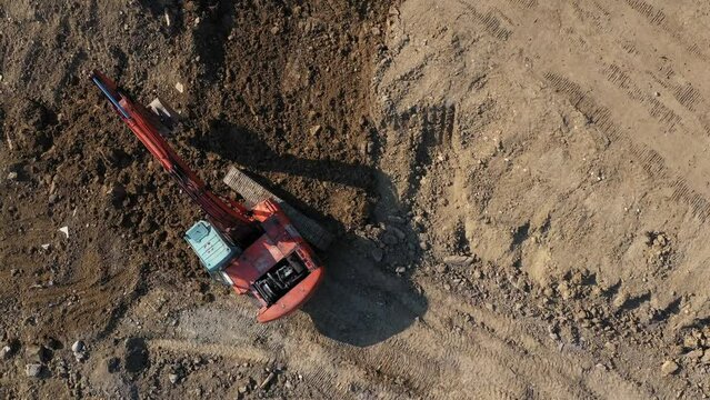 Earthmoving equipment. A red excavator is digging the ground. The bucket of the excavator scoops up the soil against the background of nature. Slow motion.