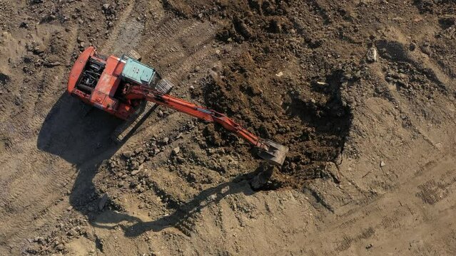 Earthmoving equipment. A red excavator is digging the ground. The bucket of the excavator scoops up the soil against the background of nature. Slow motion.