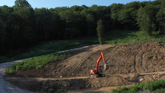 Earthmoving equipment. A red excavator is digging the ground. The bucket of the excavator scoops up the soil against the background of nature. Slow motion.