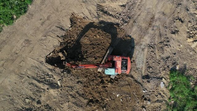 Earthmoving equipment. A red excavator is digging the ground. The bucket of the excavator scoops up the soil against the background of nature. Slow motion.