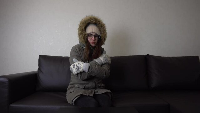A young girl sits at home on the couch in a winter jacket and freezes. The woman's electricity was cut off, and he sits upset. The poor girl didn't pay her bills.