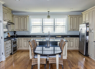 A cream colored new construction kitchen with black granite countertops and wood flooring and stainless steel appliances