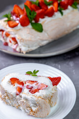 Meringue roll with strawberries. A piece of roll decorated with berries, on a white plate. Summer dessert