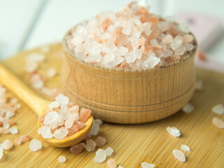 Wooden spoon and bowl with large crystals of pink Himalayan salt on a white wooden background...