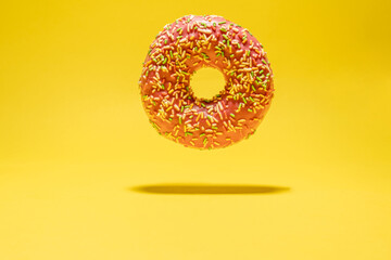 Levitating pink donut on yellow background. Creative food background