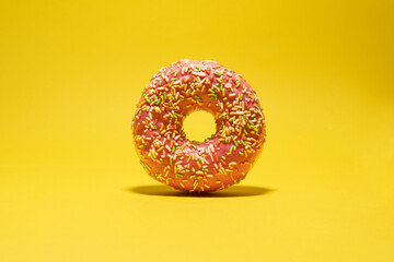 Fototapeta na wymiar Pink donut with multicolored sprinkles on yellow background. Creative food background