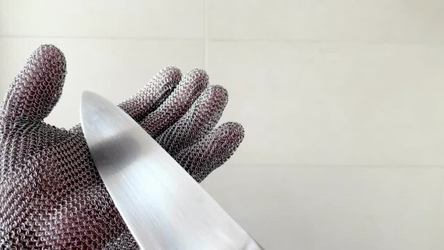 one hand with a steel mesh glove, wields a sharp stainless steel knife, protective glove for butchers with a kitchen knife, glove of metal mesh, safety at work, 4k