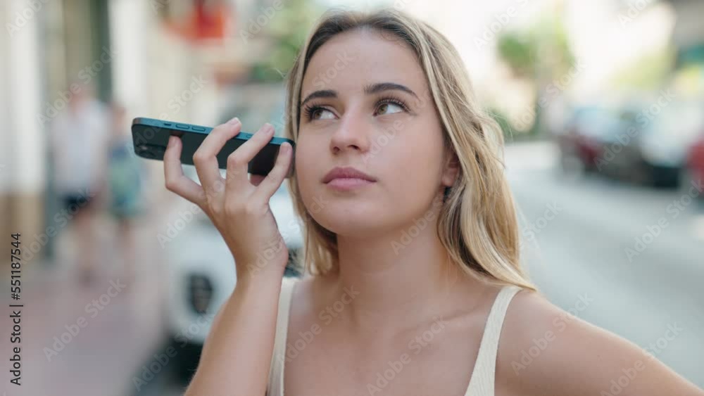 Sticker Young blonde woman listening audio message by the smartphone with serious expression at street