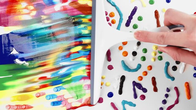 Top view male hand smears mixing multicolor paint droplets on white canvas using window squeegee. Trendy mixed colours effect, colored paint on white surface. Concept of unusual painting art workshop