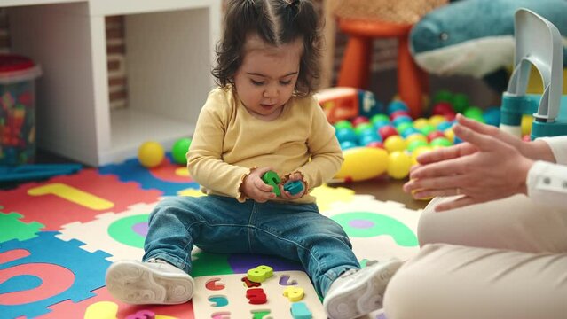 Adorable hispanic girl playing with maths puzzle game sitting on floor at kindergarten