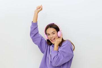 Obraz na płótnie Canvas photo of a happy woman raising her hand up and laughing with pleasure, listening to music with headphones while standing on a white studio background