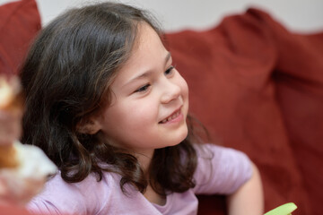 Obraz premium expressive young girl is eating chicken and vegetables for dinner on the couch while watching cartoons