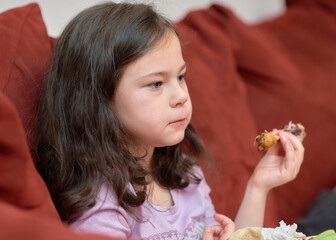 Obraz na płótnie Canvas expressive young girl is eating chicken and vegetables for dinner on the couch while watching cartoons