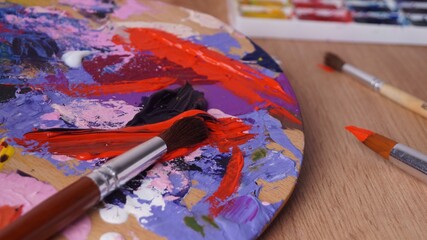 Obraz premium Artist's palette with mixed paints and brushes on wooden table