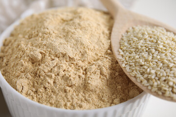 Sesame flour in bowl and wooden spoon of seeds, closeup