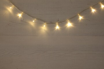 Beautiful glowing Christmas lights on white wooden table, top view. Space for text