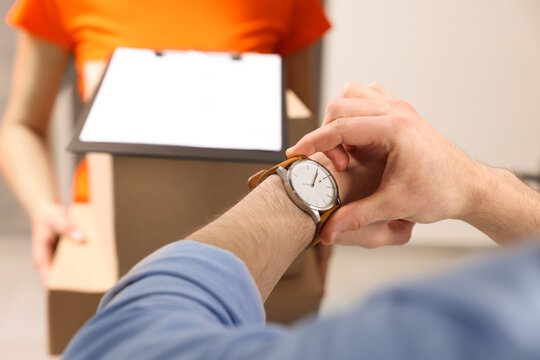 Closeup view of man checking time near courier with parcels indoors