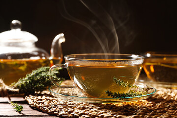 Cup of aromatic herbal tea and thyme on wooden table