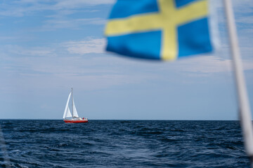 Sailboat on blue open sea with Sweden flag foreground. Concept of travel, adventure and vacation.