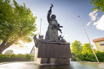 Fountain statue in the park, illuminated by the sunlight at the sunset, surrounded with green trees
