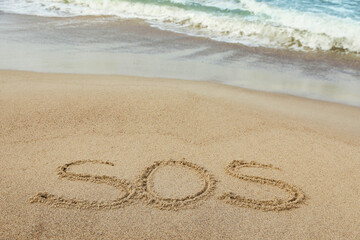 Message SOS drawn on sand near sea