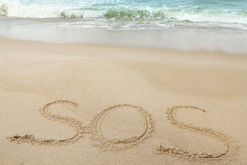Fototapeta na wymiar Message SOS drawn on sand near sea, above view