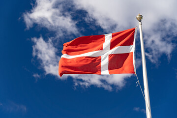 Danish flag isolated on the blue sky with clouds. Close up waving flag of Denmark.