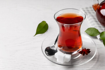 Glass of traditional Turkish tea and sugar cubes on white wooden table, closeup. Space for text
