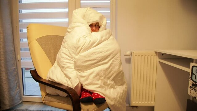 Sick woman sit in room with dim light on armchair, wrap up in warm white blanket and sneeze. Disease, chill, treatment.