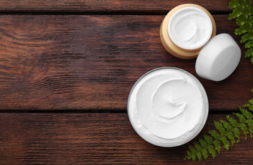 Jars of face cream and green plant on wooden table, flat lay. Space for text