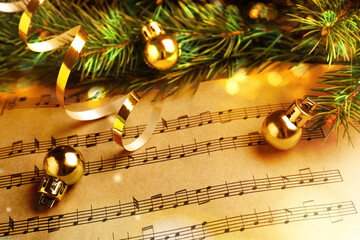 Fir branches, golden streamer and Christmas balls on music sheets, closeup