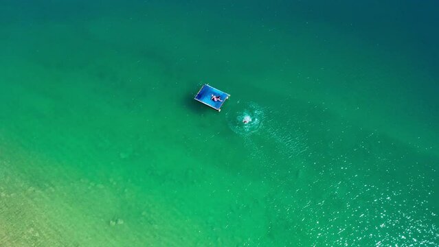 4K Mother and son have a fun on the mountain lake. They jumping into water from floating platform. Flying drone aerial footage over Peruca Lake, Dalmatia, Croatia