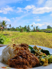 Nasi Padang contains Beef rendang, cassava leaves, spicy curry, and spicy green chilly sambal. Indonesian food, Nasi padang with beef rendang served with beautiful view. Food and nature.