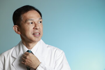 Middle-aged Asian doctor in a white coat on blue background. Concept image of regenerative medicine, vaccine development and advanced therapy.